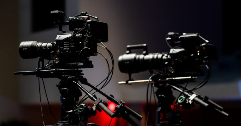 Two professional video cameras set up in a dimly lit studio environment ready for filming.
